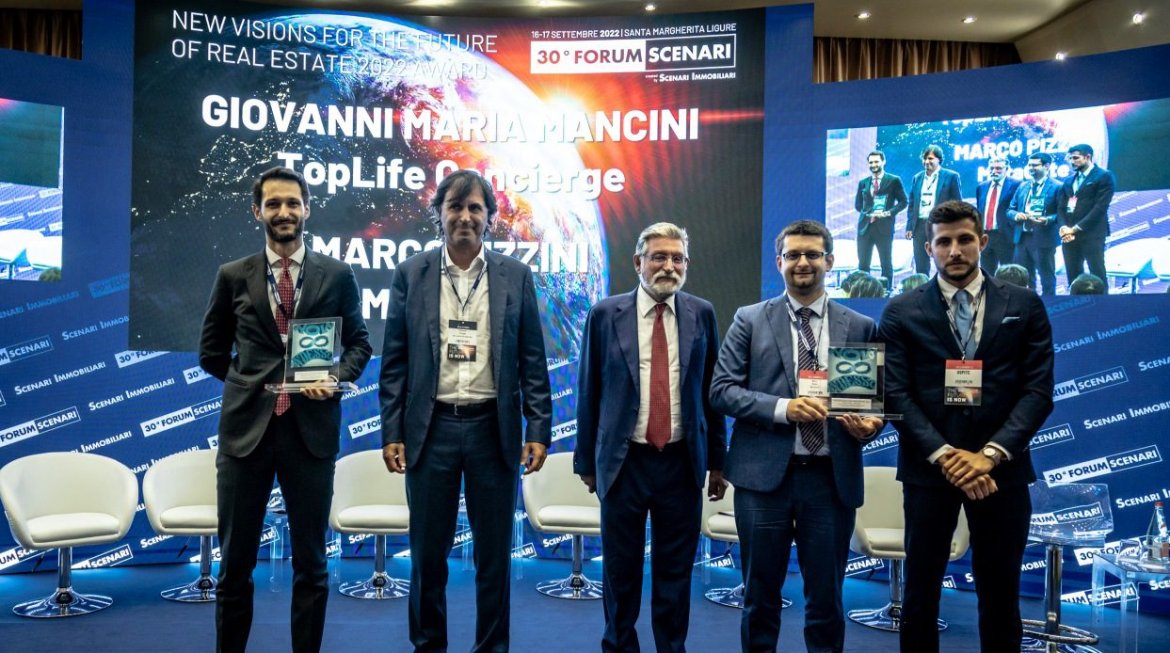 Cinque uomini in abito formale posano su un palco con uno sfondo digitale che mostra i vincitori del premio New Visions for the Future of Real Estate 2022.